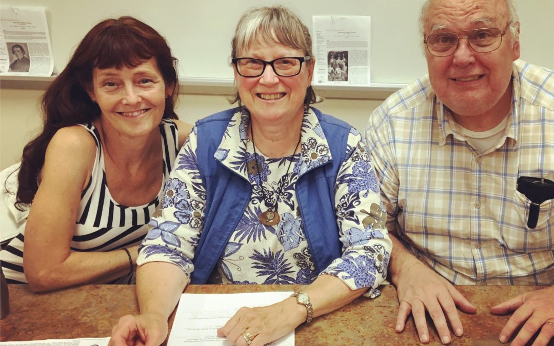 A woman, a man and a woman—three authors—sit at a table smiling in a library after a presentation. Author Cyndi Perkins is on the left.