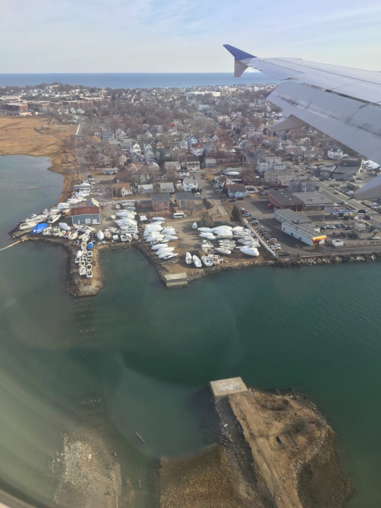 A plane wing is visible as the craft flies above Boston Harbor circling in to land at Logan International Airport. 