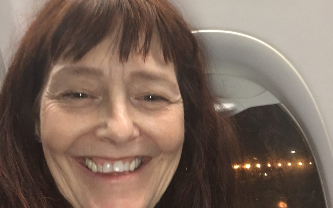 A woman smiles with the lights of an airport runway behind her.